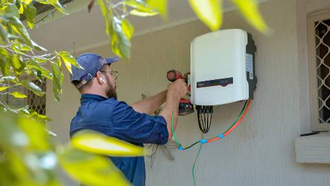 Installer fitting a wall-mounted battery and inverter unit outside a home