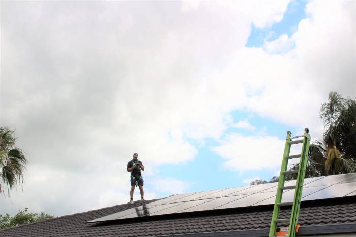 An installer working on a rooftop solar system silhouetted against a dramatic sky