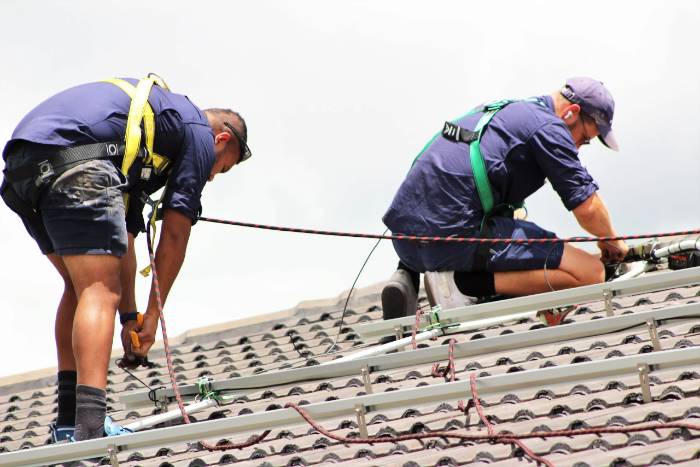 Two safety-harnessed installers working together on a tiled roof