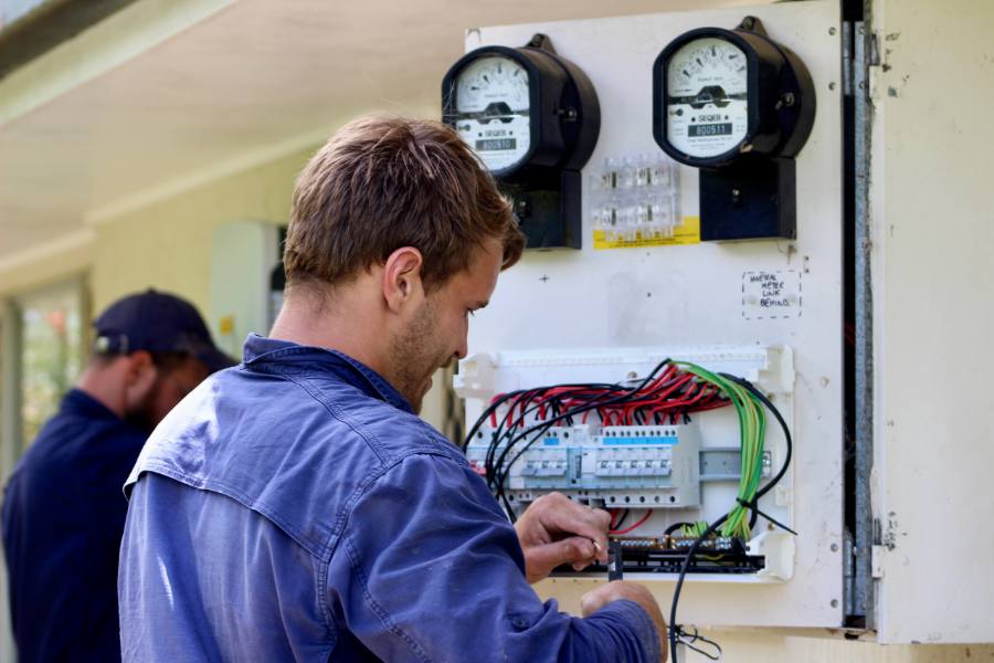 Ethos Electrical technician working inside an open switchboard, wiring multiple meters