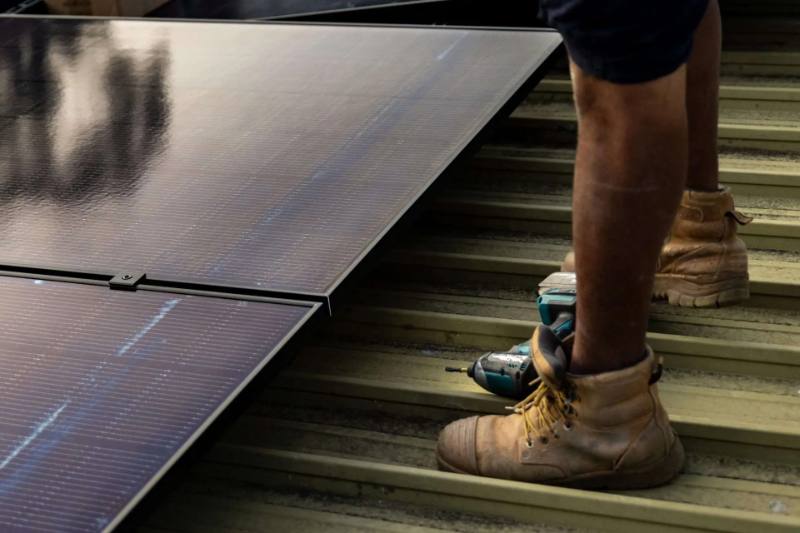 Low-angle view of an installer standing on a metal roof beside newly installed solar panels at dusk