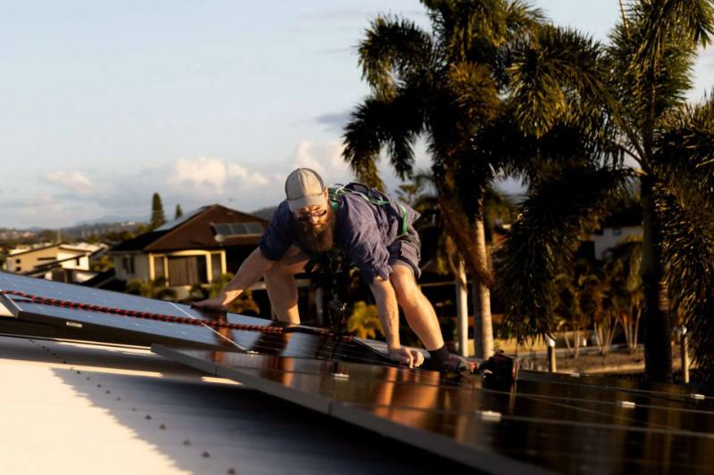 Installer crouched on a tiled roof securing a solar panel into its mounting rail