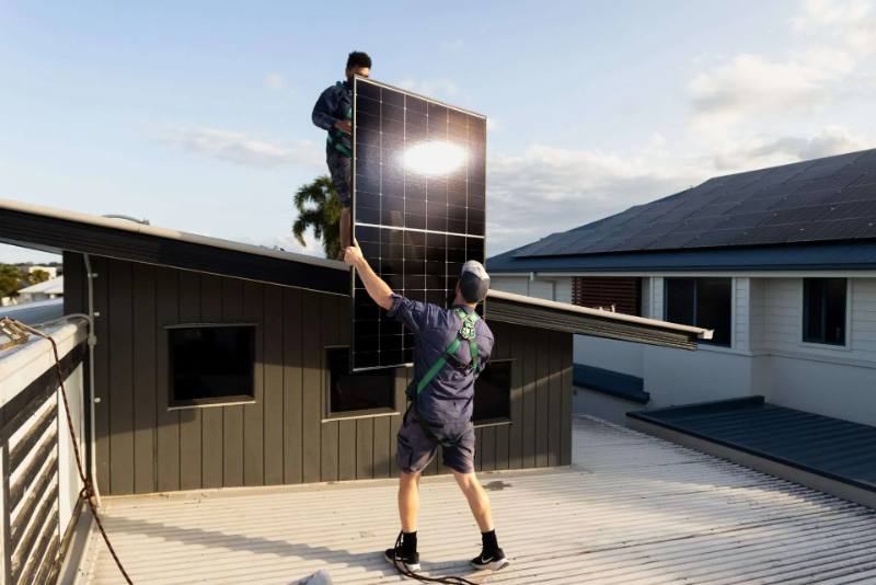 Ethos Electrical installer lifting a solar panel up onto a tiled roof