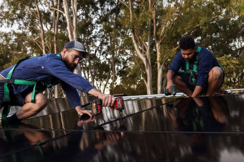 Two installers kneeling on a roof wiring solar panels together
